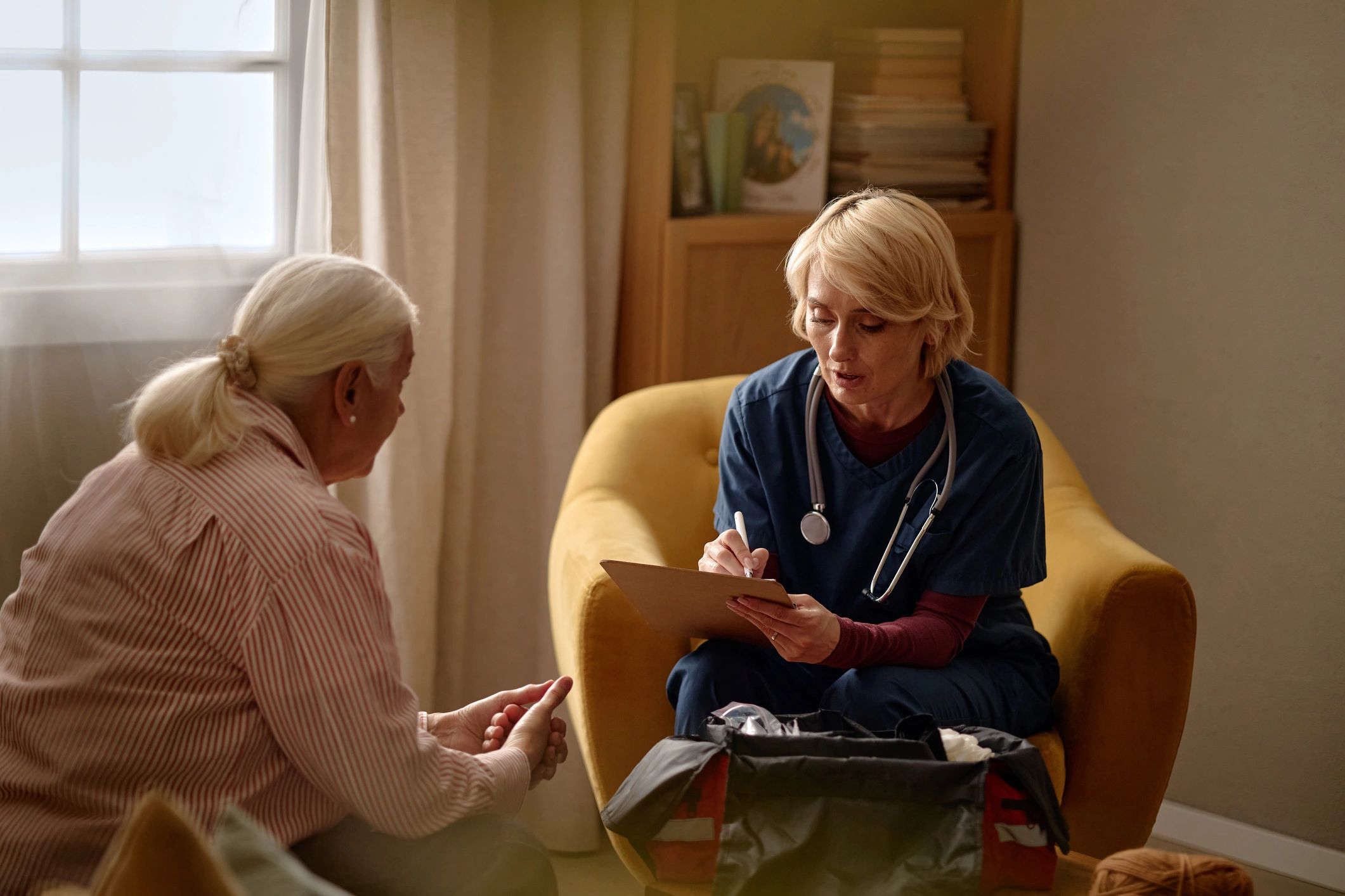 Middle aged nurse taking notes during senior woman home visit